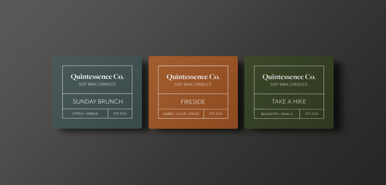 Three different iterations of a candle label containing the following information: Quintessence Co, soy wax candles, the name and various notes of the scent, and the established date. The first label, Sunday Brunch, is a deep teal color. The second, Fireside, is the same burnt orange from the business card. The third, Take a Hike, is a forest green color.